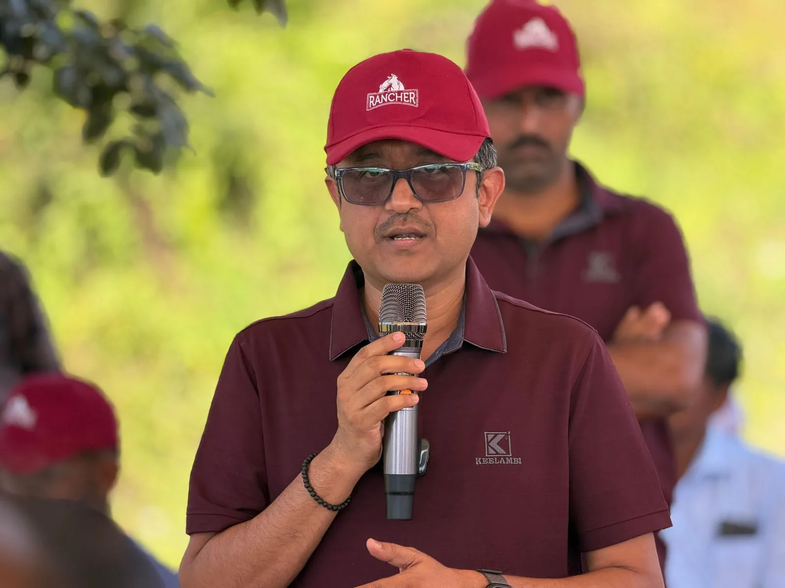 Speaker in a Rancher cap addressing the launch gathering with a microphone